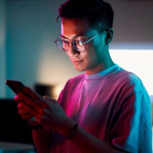 A young man wearing glasses, looking at his phone screen