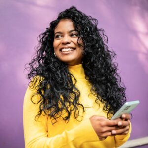 A woman in a yellow shirt holding a phone in front of a purple wall