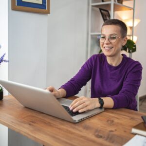 A person in a purple sweater smiling as they type on a laptop.